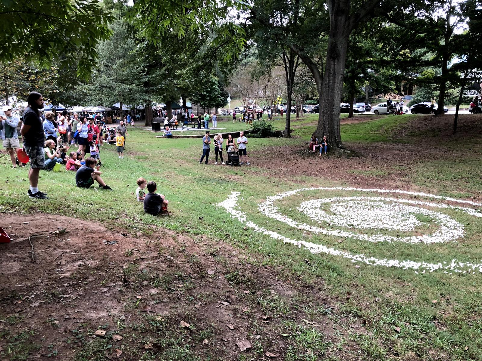 One of five durational installations created by Unexpected Collective in Grant Park: a crowd looks on as a large galaxy spiral of starch peanuts dissolves into a grass field.