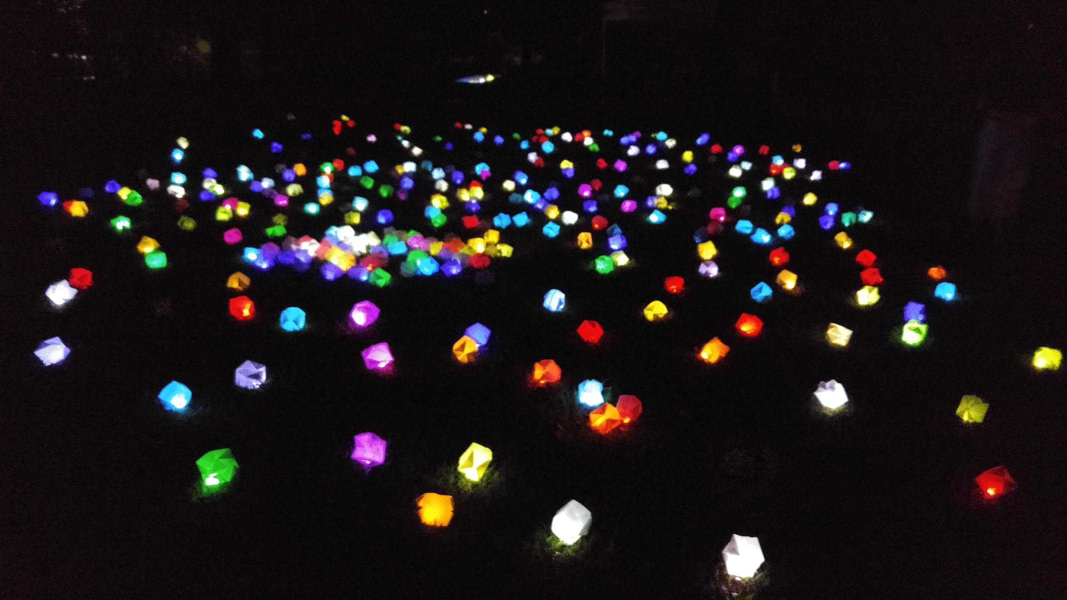 A constellation of hundreds of origami balls glow in many colors at night in a grassy area of Grant Park.