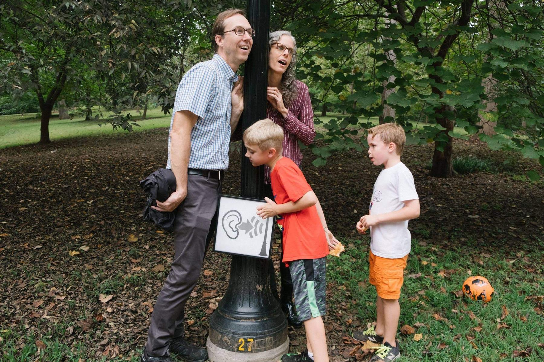 A family presses their ears agains a lamppost in Grant Park to hear historical sounds through bone conduction.
